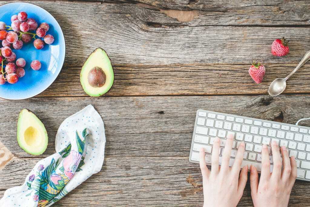 stock photo entrepreneur desk table scene with keyboard, lady hands and healthy food snacks for health coaches